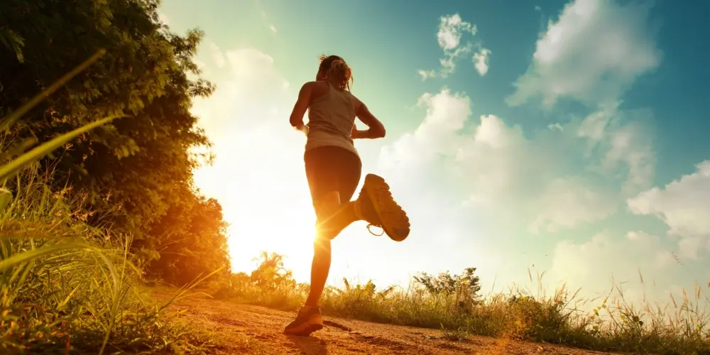 A woman is jogging on a dirt road, improving her physical and mental well-being at sunset.