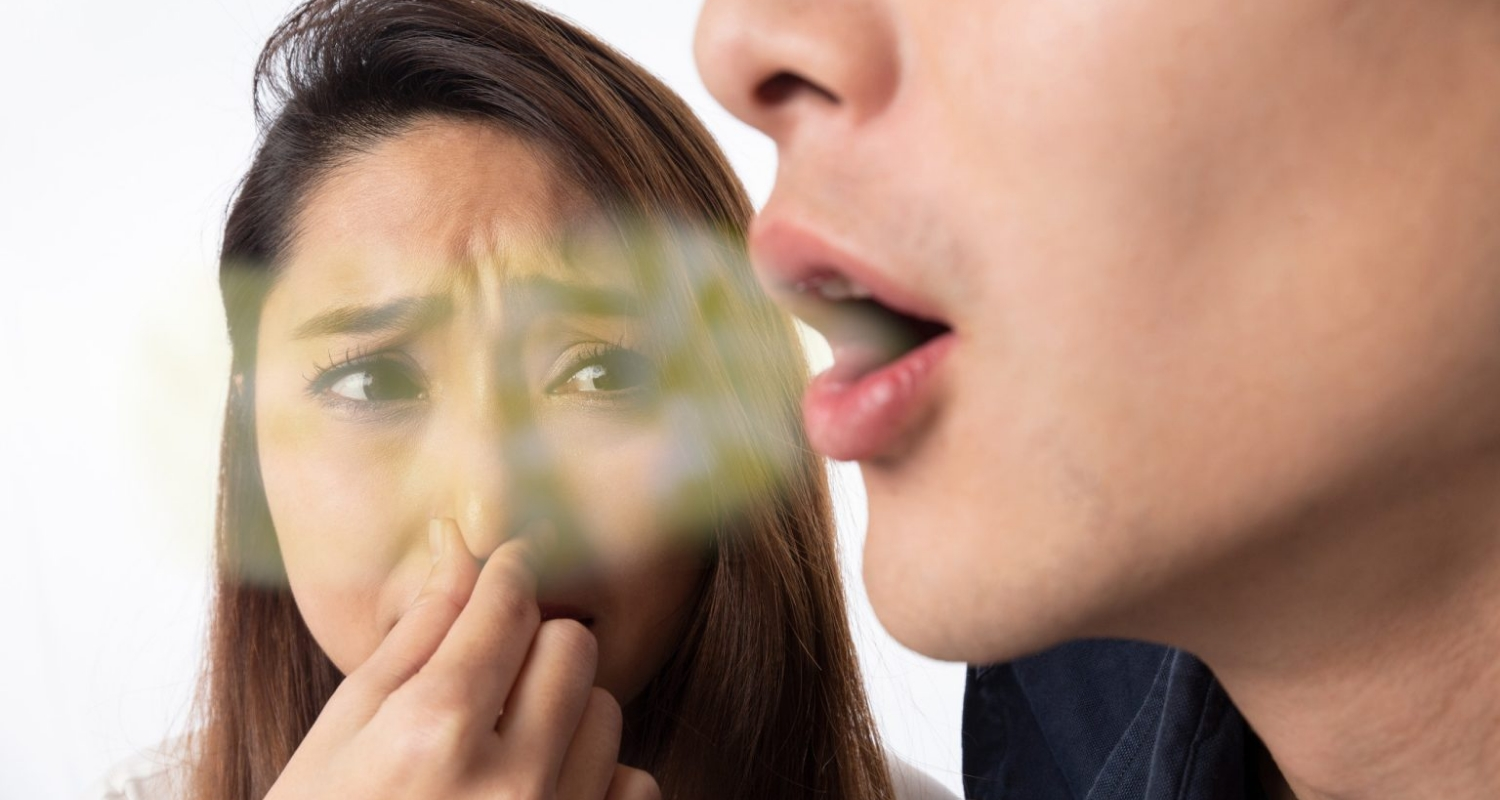 A woman grimacing and covering her nose as a man speaks close to her face, suggesting halitosis.