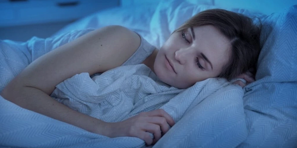 A woman is peacefully sleeping in bed, with her eyes closed, experiencing the impact of hormones on her health.