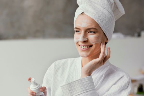  A woman in a towel is applying facial cream to her face.