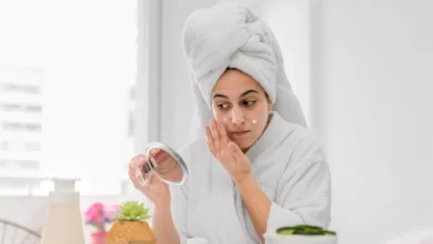 A woman in a bathrobe applying a facial mask to her face for a rejuvenating skincare routine.